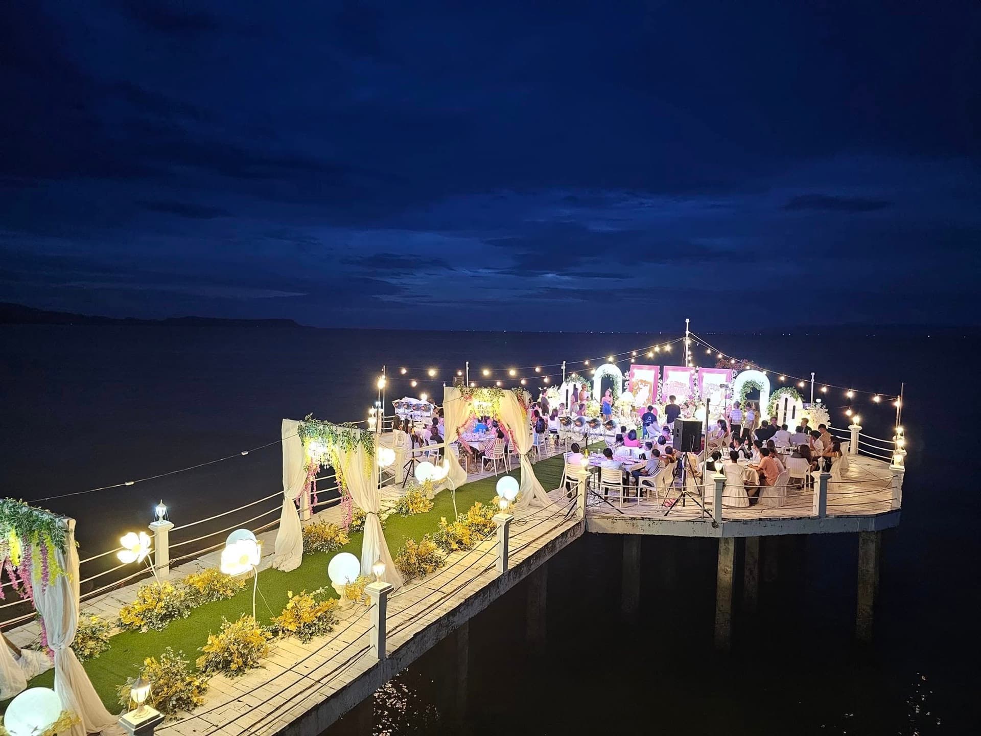 A wedding on the lit pier and jetty event deck over the bay at dusk at Cherish Resort, Masbate City